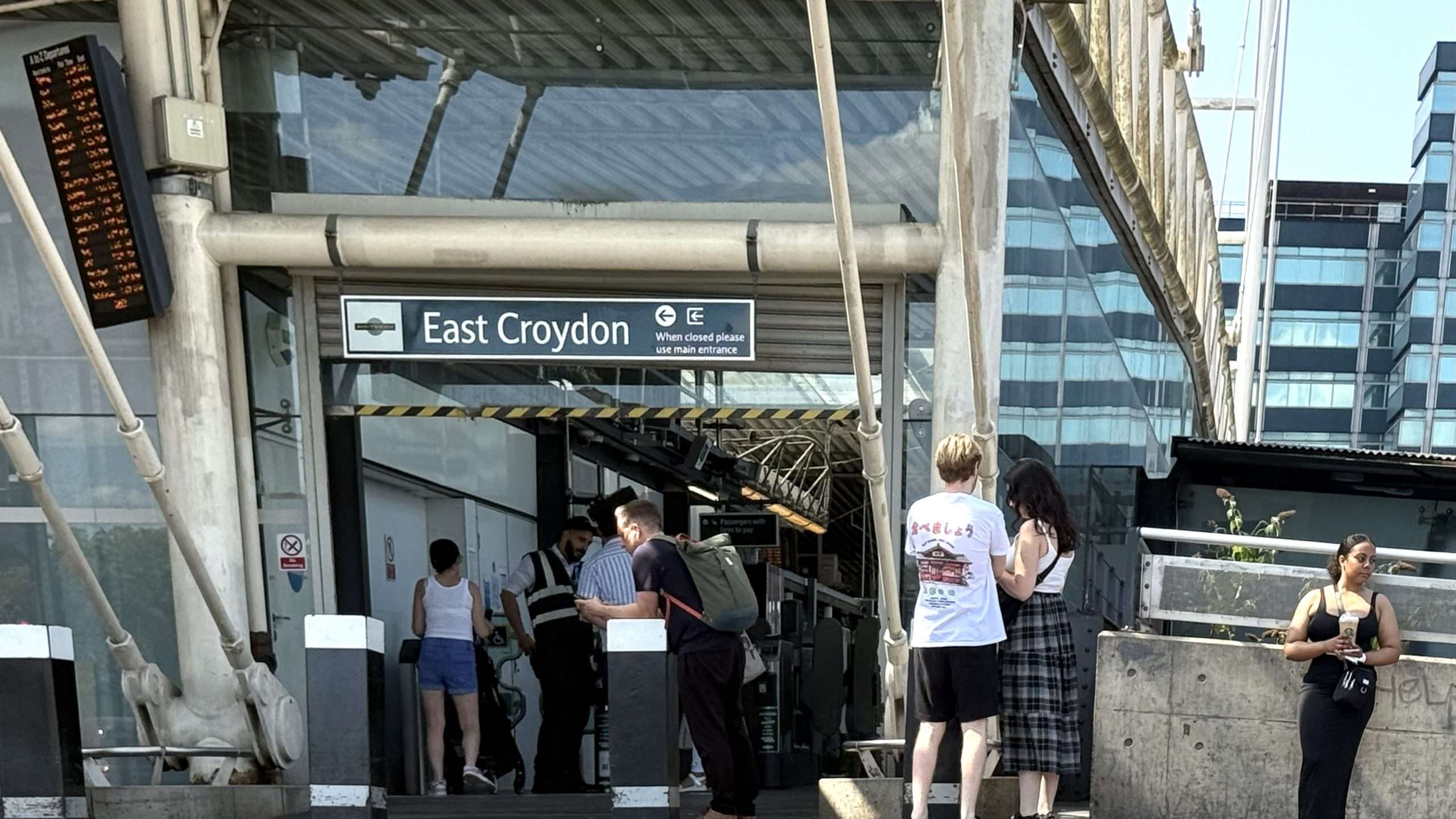 “East Croydon Station entrance with passengers, station sign, and modern glass building in the background”